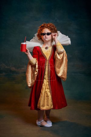Portrait of little red-headed girl in costume of royal person posing in sunglasses and soda isolated on dark green background. Concept of historical remake, comparison of eras, medieval fashion, queen