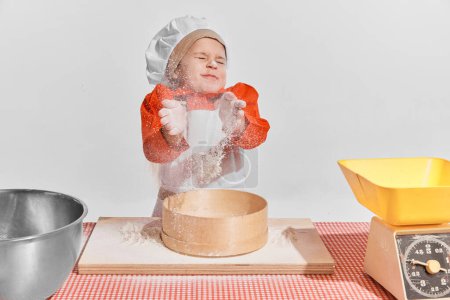 Photo for Cute little child, girl in image of chef cooking over grey background. Sifting flour, dirty face. Concept of childhood, creativity, retro style, vintage fashion, future profession, friendship, art - Royalty Free Image