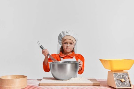 Photo for Cute little child, girl in image of chef cooking over grey background. Mixing dough. Concept of childhood, creativity, retro style, vintage fashion, future profession, friendship, art - Royalty Free Image
