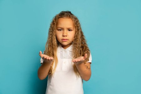 Photo for Resentment. Sad little girl, kid with long hair wearing white t-shirt expressing emotions isolated over blue background. Concept of children emotions, fashion, beauty, back to school, ad - Royalty Free Image