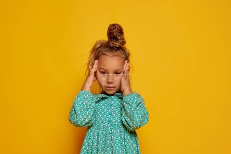Photo for Partial image of serious little girl looking at camera. Portrait of beautiful caucasian female child with headache. Childhood concept. Isolated on yellow studio background. Copy space for ad - Royalty Free Image
