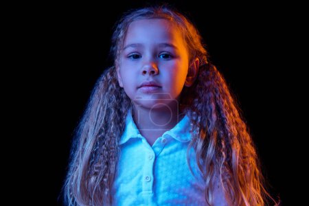 Photo for Resentment. Sad little girl, kid with long hair wearing white t-shirt expressing emotions isolated over black background in neon light. Concept of children emotions, fashion, beauty, back to school - Royalty Free Image