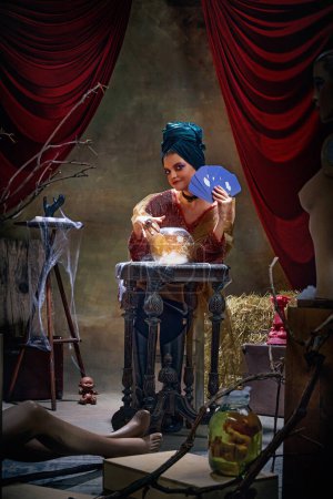 Photo for Portrait of magnificent fortune teller woman reading future on magical crystal ball and tarot cards over dark circus backstage background. Concept of vintage style, retro circus, art, fate - Royalty Free Image