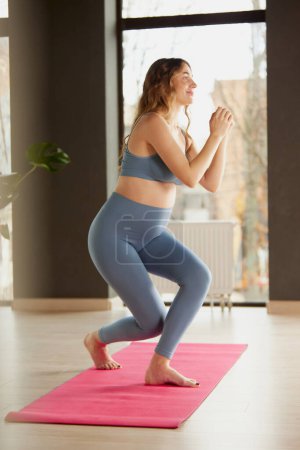 Photo for Portrait of young pregnant woman doing yoga on mat in comfortable sportswear indoors on a daytime. Squats. Concept of motherhood, health care, sportive lifestyle, fitness, wellness, pregnancy - Royalty Free Image