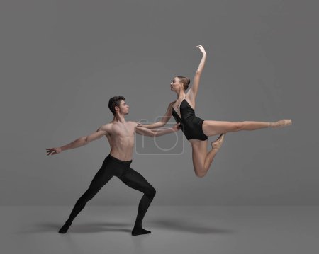 Young man and woman, ballet dancers performing isolated over dark grey studio background. Jumping high. Concept of classical dance aesthetics, choreography, art, beauty. Copy space for ad