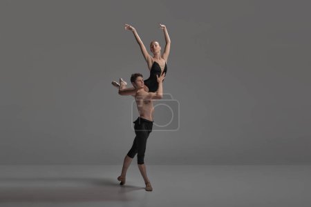 Joven y mujer, bailarines de ballet actuando aislados sobre fondo de estudio gris oscuro. Manteniendo el equilibrio en el hombro. Concepto de danza clásica estética, coreografía, arte, belleza. Copiar espacio para anuncio