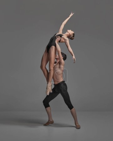 Young man and woman, ballet dancers performing isolated over dark grey studio background. Growing high. Concept of classical dance aesthetics, choreography, art, beauty. Copy space for ad