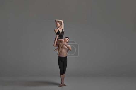Téléchargez les photos : Jeune homme et jeune femme, danseurs de ballet se produisant isolés sur fond de studio gris foncé. Assis sur une épaule. Concept de danse classique esthétique, chorégraphie, art, beauté. Espace de copie pour la publicité - en image libre de droit