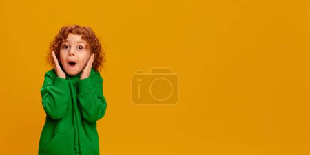 Téléchargez les photos : Portrait de mignonne petite fille, enfant aux cheveux roux bouclés posant avec une expression choquée isolée sur fond jaune. Concept d'enfance, émotions, mode de vie, mode, bonheur. Espace de copie pour la publicité - en image libre de droit