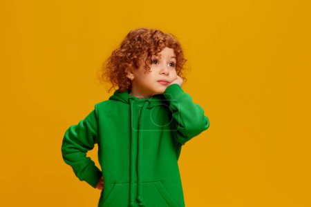 Photo for Portrait of cute little girl, child with curly red hair posing with bored face isolated over yellow background. Concept of childhood, emotions, lifestyle, fashion, happiness. Copy space for ad - Royalty Free Image