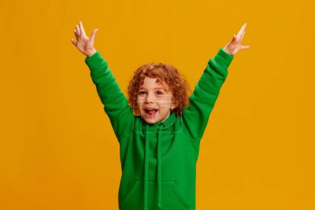 Photo for Portrait of cute little girl, child with curly red hair posing with cheerful look isolated over yellow background. Concept of childhood, emotions, lifestyle, fashion, happiness. Copy space for ad - Royalty Free Image