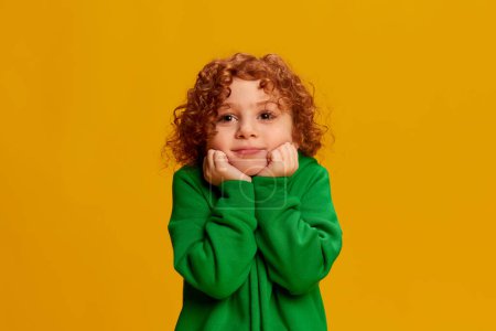 Photo for Portrait of cute little girl, child with curly red hair posing isolated over yellow background. Angel face. Concept of childhood, emotions, lifestyle, fashion, happiness. Copy space for ad - Royalty Free Image