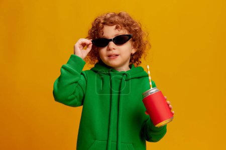 Photo for Portrait of cute stylish little girl, child with curly red hair posing in sunglasses isolated over yellow background. Concept of childhood, emotions, lifestyle, fashion, happiness. Copy space for ad - Royalty Free Image