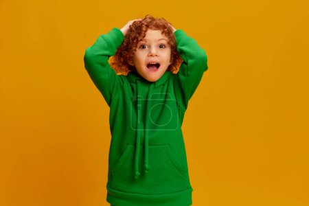 Photo for Portrait of little girl, child with curly red hair posing with shocked face isolated over yellow background. Surprise. Concept of childhood, emotions, lifestyle, fashion, happiness. Copy space for ad - Royalty Free Image