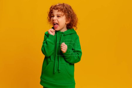 Photo for Portrait of cute little girl, child with curly red hair posing, shouting isolated over yellow background. Concept of childhood, emotions, lifestyle, fashion, happiness. Copy space for ad - Royalty Free Image