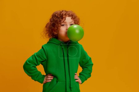 Photo for Portrait of cute little girl, child with curly red hair posing with big bubble gum isolated over yellow background. Concept of childhood, emotions, lifestyle, fashion, happiness. Copy space for ad - Royalty Free Image