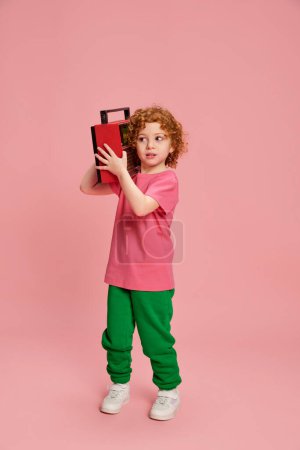 Photo for Portrait of cute little girl, child with curly red hair posing with music player isolated over pink background. Concept of childhood, emotions, lifestyle, fashion, happiness. Copy space for ad - Royalty Free Image