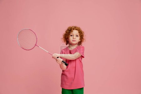 Photo for Portrait of cute little girl, child with curly red hair playing badminton isolated over pink background. Concept of childhood, emotions, lifestyle, fashion, happiness. Copy space for ad - Royalty Free Image