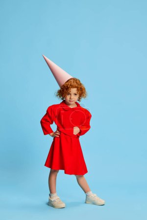 Foto de Linda niña, niño con el pelo rojo rizado posando en traje de un hada aislado sobre fondo azul. Cumpleaños. Concepto de infancia, emociones, estilo de vida, moda, felicidad. Copiar espacio para anuncio - Imagen libre de derechos