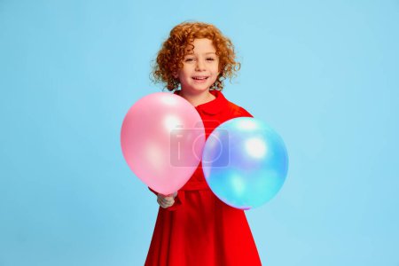Photo for Portrait of cute little girl, child with curly red hair posing with balloons isolated on blue background. Birthday kid. Concept of childhood, emotions, lifestyle, fashion, happiness. Copy space for ad - Royalty Free Image