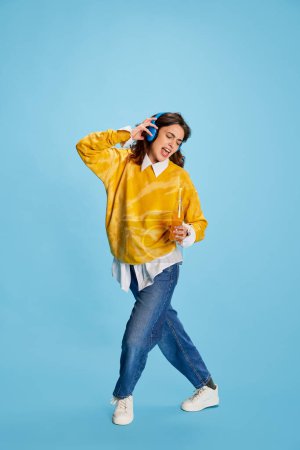 Photo for Portrait of young beautiful girl in casual clothes listening to music in headphones isolated over blue background. Concept of youth, beauty, fashion, lifestyle, emotions, facial expression. Ad - Royalty Free Image