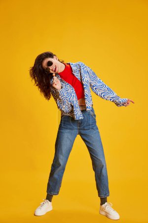 Photo for Portrait of young beautiful girl posing in stylish clothes, singing isolated over yellow background. Concept of youth, beauty, fashion, lifestyle, emotions, facial expression. Ad - Royalty Free Image