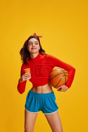 Photo for Portrait of young beautiful girl posing in comfortable sportswear with basketball ball isolated over yellow background. Concept of youth, beauty, sport lifestyle, emotions, facial expression. Ad - Royalty Free Image