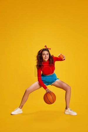 Photo for Portrait of young beautiful girl with curly hair posing, dribbling basketball ball isolated over yellow background. Concept of youth, beauty, sport lifestyle, emotions, facial expression. Ad - Royalty Free Image