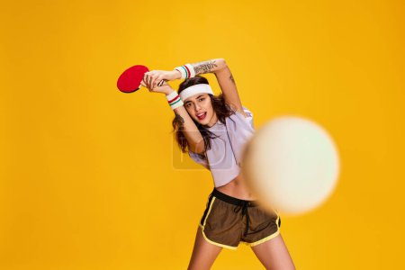 Téléchargez les photos : Portrait de jeune fille émotive posant, jouant au tennis de table isolé sur fond jaune. Action, motion. Concept de jeunesse, beauté, style de vie sportif, émotions, expression faciale. Publicité - en image libre de droit