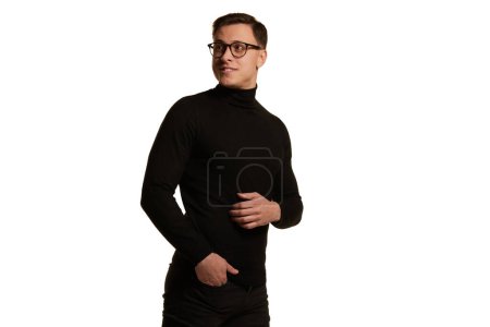 Téléchargez les photos : Portrait de bel homme d'affaires élégant en tenue noire totale portant des lunettes posant isolé sur fond blanc. Concept de beauté, de mode, de style et d'affaires. Émotions positives et santé mentale - en image libre de droit
