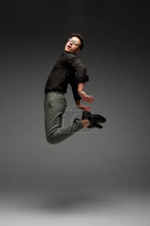 Photo for Freedom. Happy young man, student, business in black classic style shirt and grey trousers running, jumping isolated over grey background. Modern office style, emotions, active lifestyle - Royalty Free Image