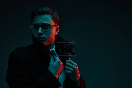 Photo for Studio shot of serious young 30s years old man in classic style clothes posing isolated over dark background in neon light. Fashion, style, emotions concept. Mental health, diversity, freedom - Royalty Free Image