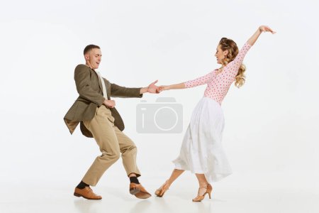 Dos bailarines emocionales en ropa de estilo vintage bailando swing dance, rock-and-roll aislados sobre fondo blanco. Tradiciones atemporales, estilo y arte de la moda americana de 1960. Pareja mirada feliz, encantado