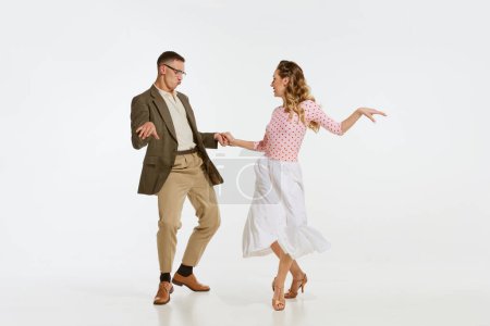 Foto de Amor en movimiento. Joven emocionado hombre y mujer que lleva ropa de estilo americano de los años 60 bailando danza retro aislada sobre fondo blanco. Música, energía, felicidad, humor, acción - Imagen libre de derechos