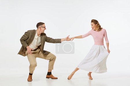 Love in motion. Young excited man and woman wearing 60s american fashion style clothes dancing retro dance isolated on white background. Music, energy, happiness, mood, action