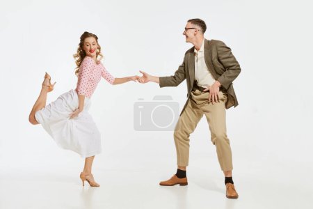 Dos bailarines emocionales en ropa de estilo vintage bailando swing dance, rock-and-roll aislados sobre fondo blanco. Tradiciones atemporales, estilo y arte de la moda americana de 1960. Pareja mirada feliz, encantado