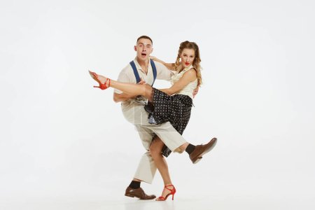 Two emotional dancers in vintage style clothes dancing swing dance, rock-and-roll isolated on white background. Timeless traditions, 1960s american fashion style and art. Couple look happy, delighted
