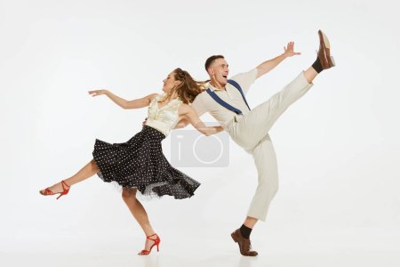Téléchargez les photos : L'amour en mouvement. Jeune homme excité et femme portant des vêtements de style mode américaine des années 60 dansant danse rétro isolé sur fond blanc. Musique, énergie, bonheur, humeur, action - en image libre de droit