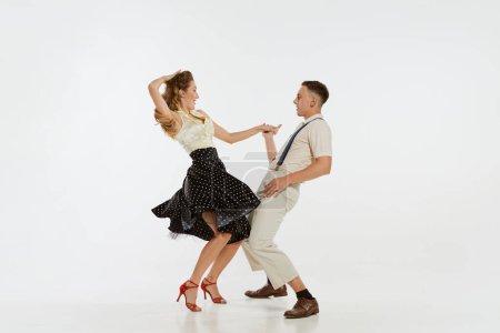 Two emotional dancers in vintage style clothes dancing swing dance, rock-and-roll isolated on white background. Timeless traditions, 1960s american fashion style and art. Couple look happy, delighted