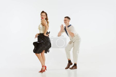 Téléchargez les photos : L'amour en mouvement. Jeune homme excité et femme portant des vêtements de style mode américaine des années 60 dansant danse rétro isolé sur fond blanc. Musique, énergie, bonheur, humeur, action - en image libre de droit