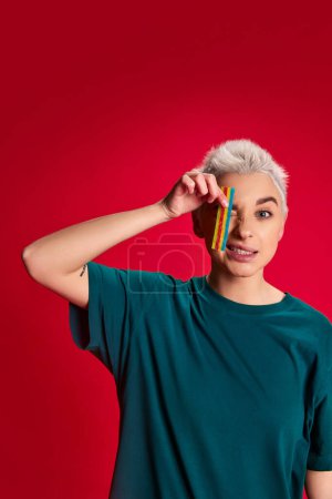 Photo for Portrait of young stylish woman with short hair posing with jelly candy isolated over red background. Sweet tooth. Concept of youth, beauty, fashion, lifestyle, emotions, facial expression. Ad - Royalty Free Image