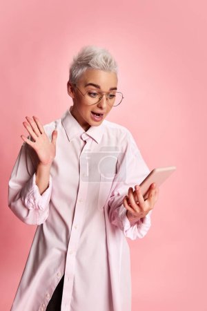 Photo for Portrait of young stylish woman with short hair posing with phone isolated over pink background. Online shopping. Concept of youth, beauty, fashion, lifestyle, emotions, facial expression. Ad - Royalty Free Image