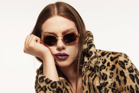 Photo for Portrait of beautiful woman posing in trendy sunglasses and animal print coat over white background. Plum colored lipstick. Bored look. Concept of style, beauty, high fashion, magazine style and ad - Royalty Free Image