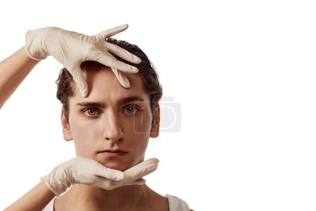 Photo for Portrait of young man and female hands in gloves on male face isolated over white background. Concept of male beauty, skincare, plastic surgery, cosmetology, health. Copy space for ad - Royalty Free Image