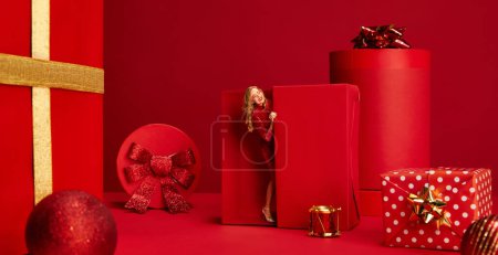 Photo for CStylish beautiful woman in sparkling dress appearing from present box over red background. Valentines day. Concept of holidays, celebration, presents, greetings. shopping, sales. Copy space for ad - Royalty Free Image
