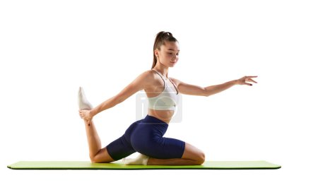 Photo for Portrait of young sportive woman training, doing stretching exercises on sport mat isolated over white background. Concept of sport, strength, body care, fitness, wellbeing, health. Ad - Royalty Free Image