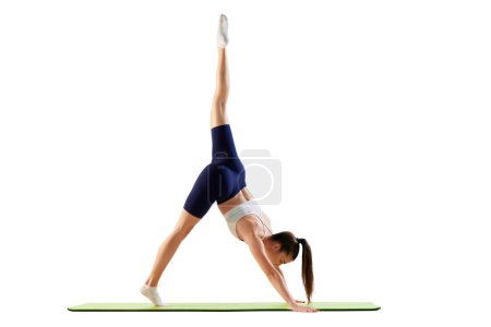 Photo for Portrait of young sportive woman training, doing stretching exercises, rising leg up, body down isolated over white background. Concept of sport, strength, body care, fitness, wellbeing, health. Ad - Royalty Free Image