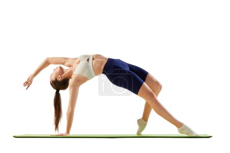 Photo for Portrait of young sportive woman training, doing full-body stretching exercises on mat isolated over white background. Concept of sport, strength, body care, fitness, wellbeing, health. Ad - Royalty Free Image