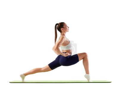Foto de Retrato de una joven entrenadora deportiva, haciendo ejercicios de estiramiento de piernas sobre una esterilla aislada sobre fondo blanco. Concepto de deporte, fuerza, cuidado corporal, fitness, bienestar, salud. Anuncio - Imagen libre de derechos
