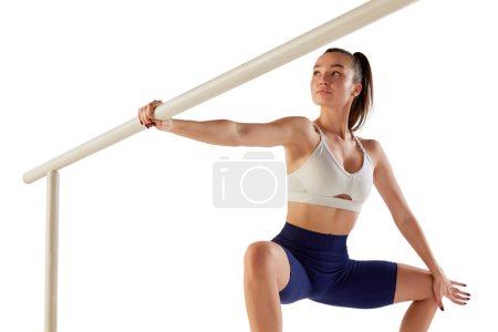 Foto de Retrato de una joven entrenadora deportiva, haciendo sentadillas, sosteniendo una barra de ballet aislada sobre fondo blanco. Concepto de deporte, fuerza, cuidado corporal, fitness, bienestar, salud. Anuncio - Imagen libre de derechos